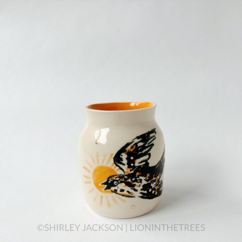 Ceramic vase featuring an experimental Barn Swallow motif. This vase has orange underglaze on the inside and gold overglaze around the vase.