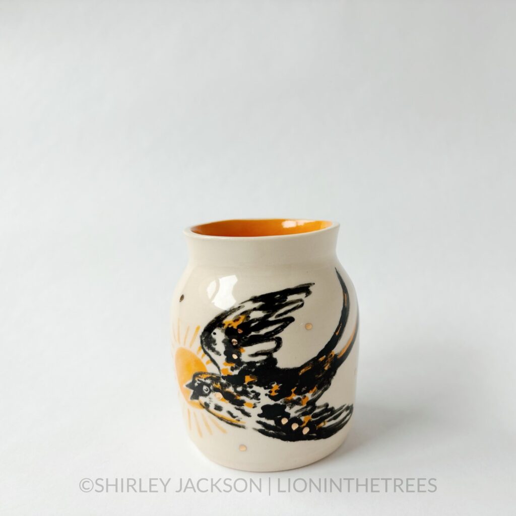 Ceramic vase featuring an experimental Barn Swallow motif. This vase has orange underglaze on the inside and gold overglaze around the vase.