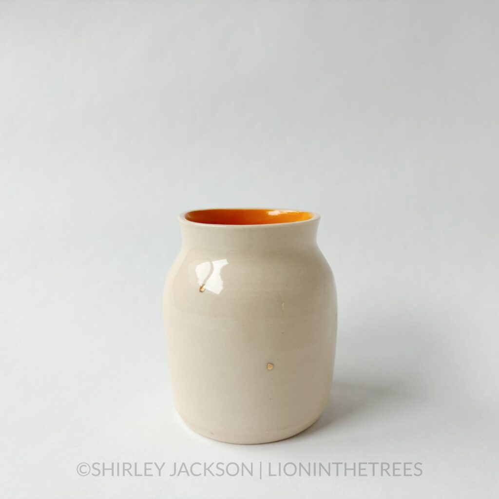 Ceramic vase featuring an experimental Barn Swallow motif. This vase has orange underglaze on the inside and gold overglaze around the vase.