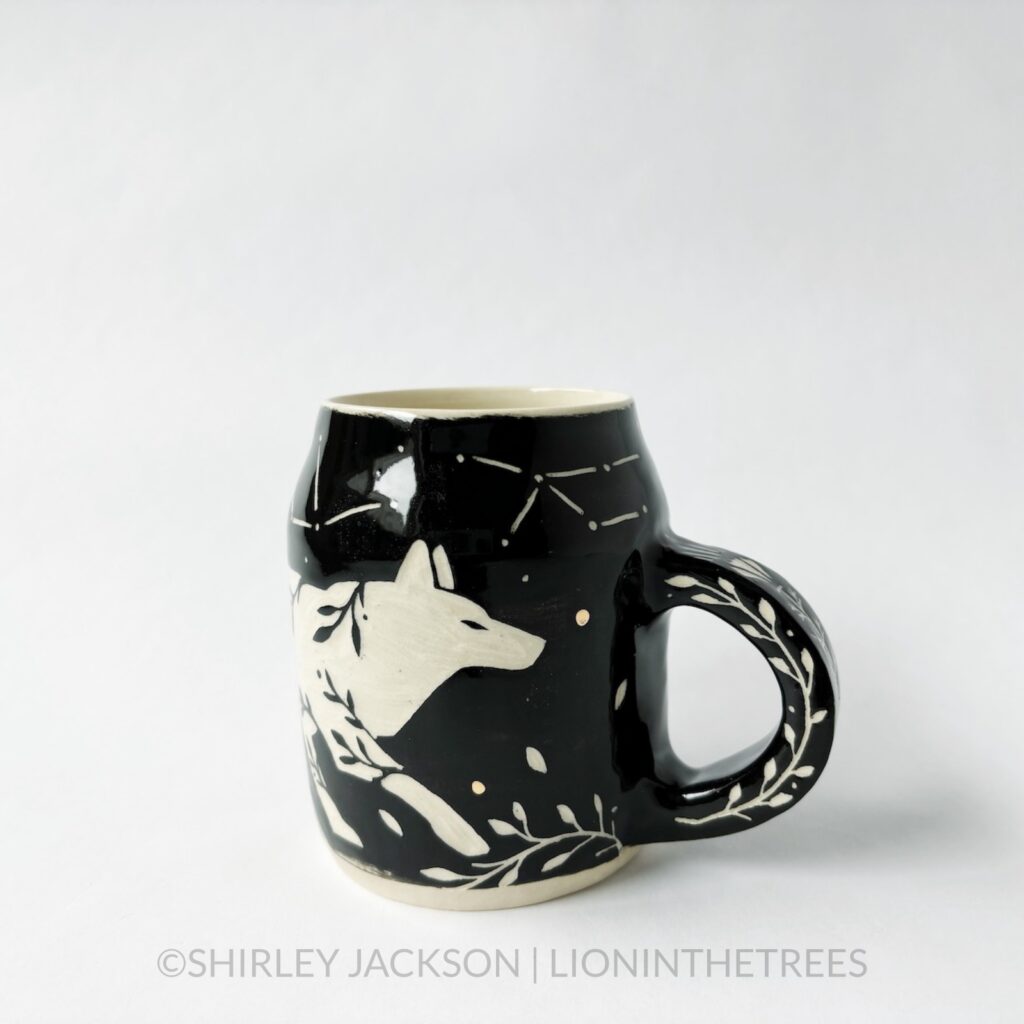 Ceramic black sgraffito mug featuring my Running Wolf motif. This mug also features a floral border above and below the Wolf motif.