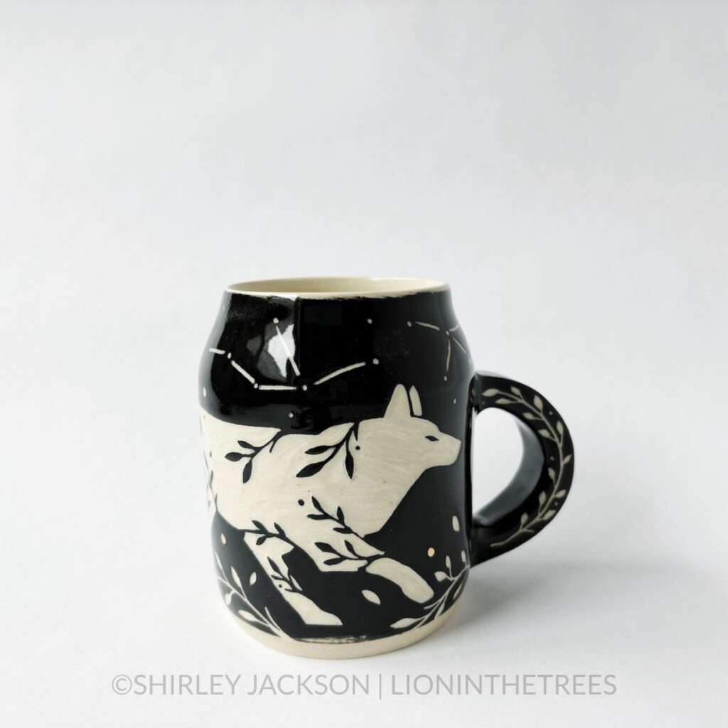 Ceramic black sgraffito mug featuring my Running Wolf motif. This mug also features a floral border above and below the Wolf motif.