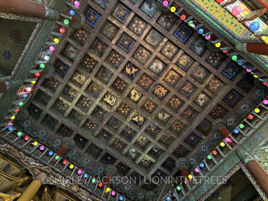 Worm's eye view of the ceiling of the Buddha temple. There are a variety of square tiles that have beautiful designs featuring cranes, dragons, and more.
