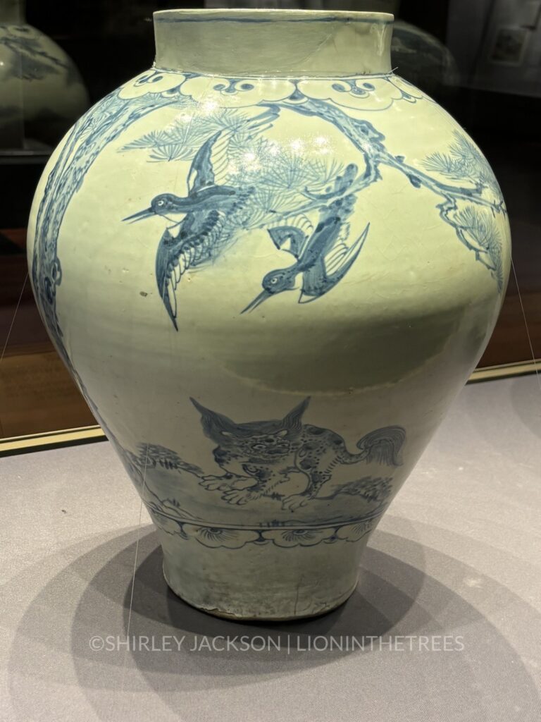 A bird painted vase with a little grimlin looking creature on the bottom