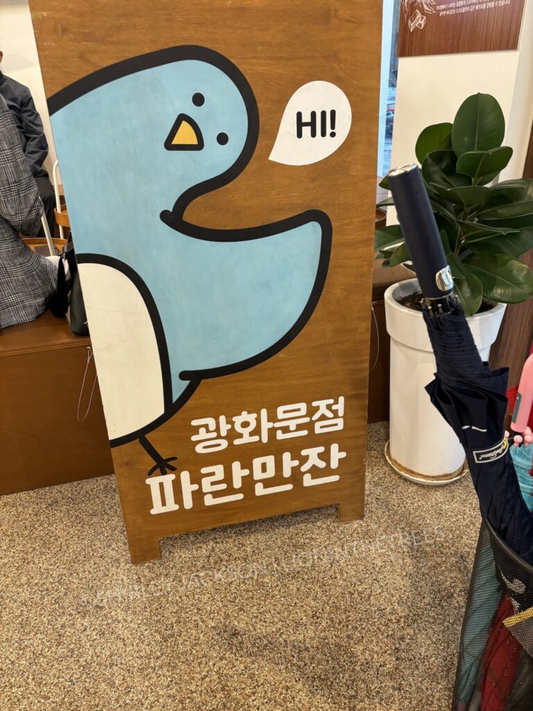 A photo of the cafe's blue bird mascot waving and saying "Hi!"