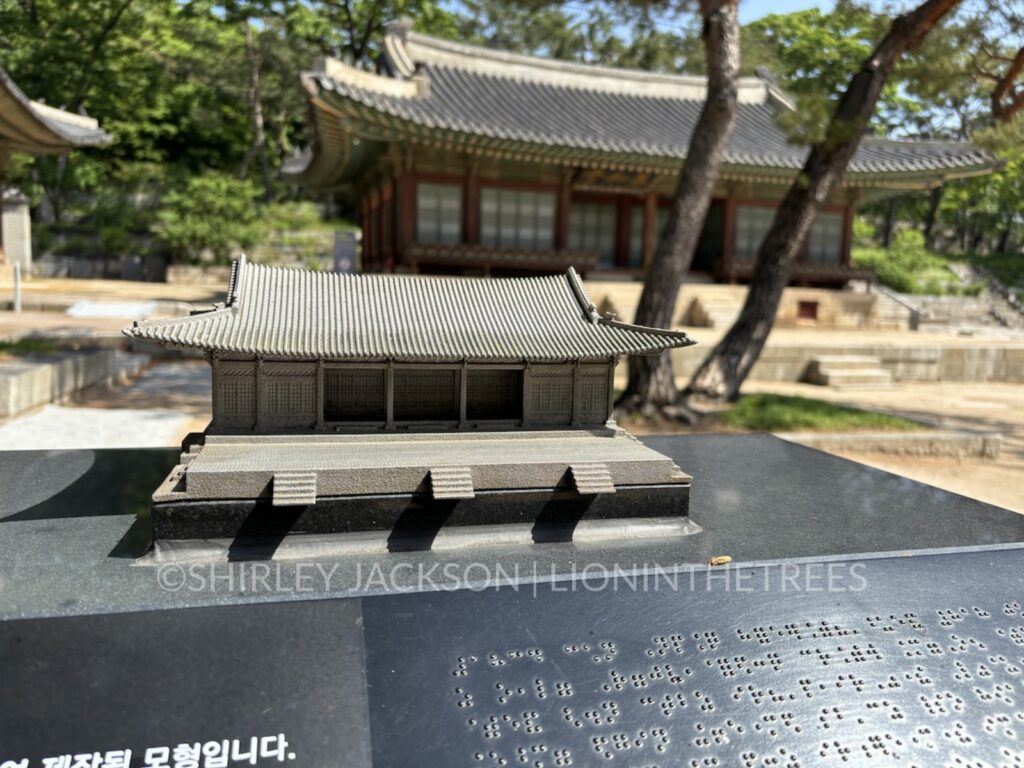 A small scale replica of the queen's palace with the actual building behind it.