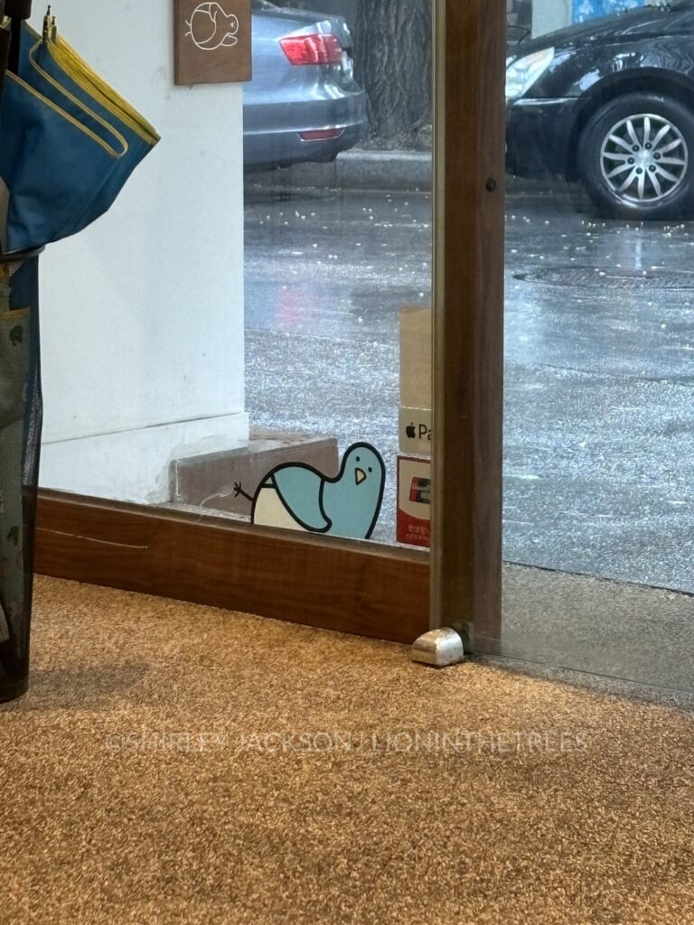 Photo of the little blue bird mascot as a sticker on the window where they appear to be resting on the window ledge.