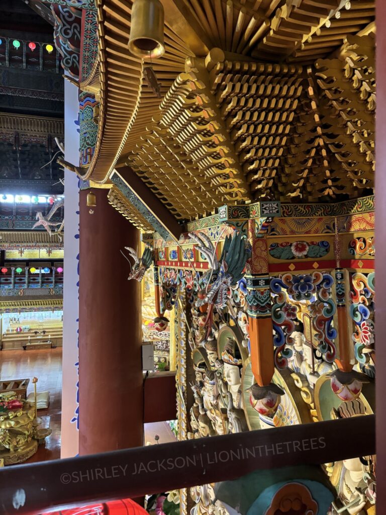 Photo inside the Buddha temple showing the golden architecture and dragon heads hanging from the side of this wall