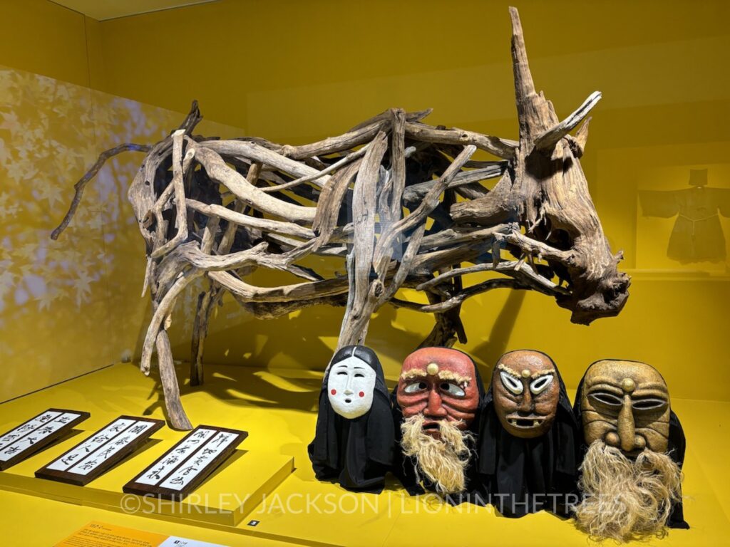 Photo of a large boar-like creature made out of drift wood along with a series of masks