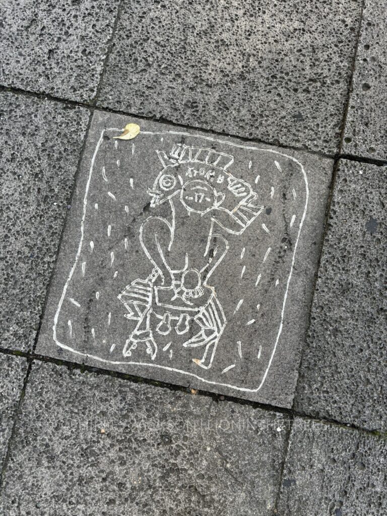 art found on the sidewalk of jeju island portraying a nude figure standing on top of a crab hoisting a fish over their head