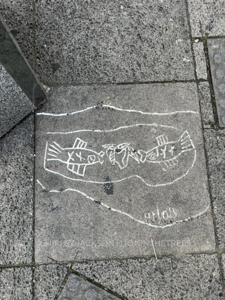 art found on the sidewalk of jeju island portraying two fish facing each other and what appears to be an apple or some kind of fruit in-between them