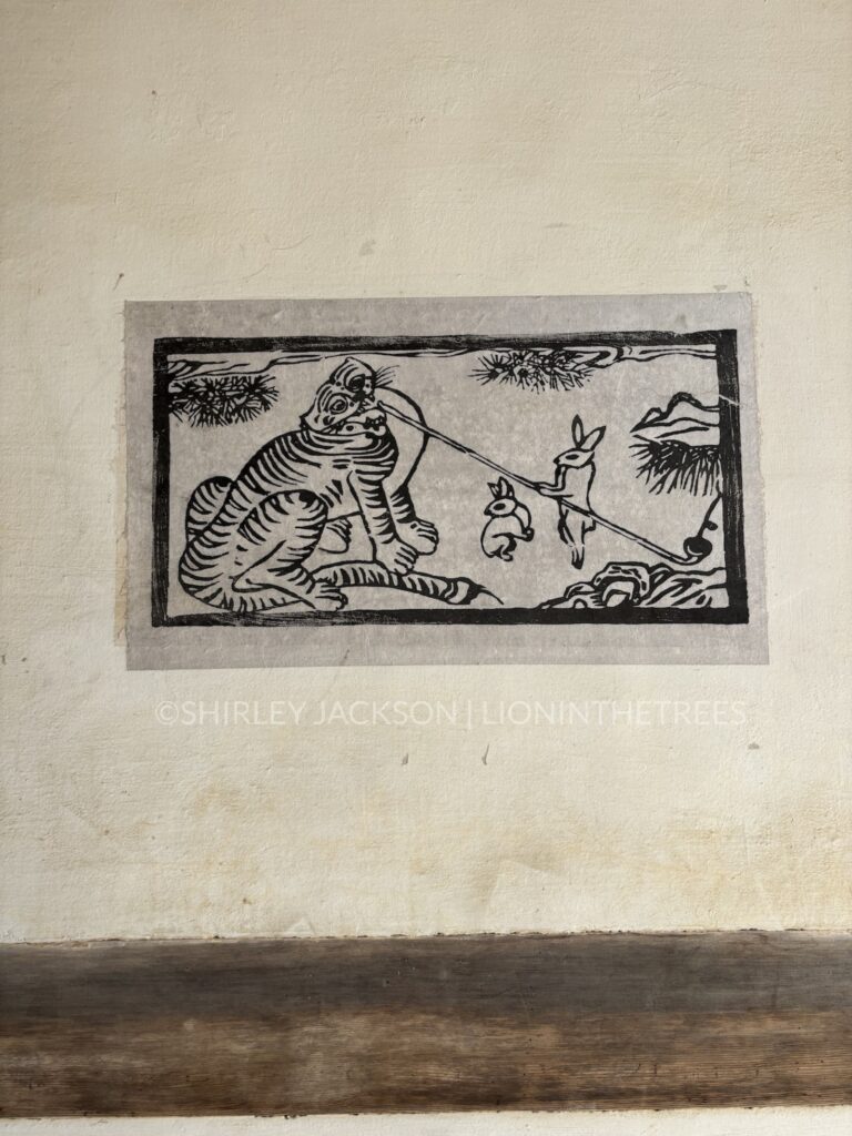 Photo of a woodblock tiger design wherein they're smoking a pipe with the help of two rabbit friends