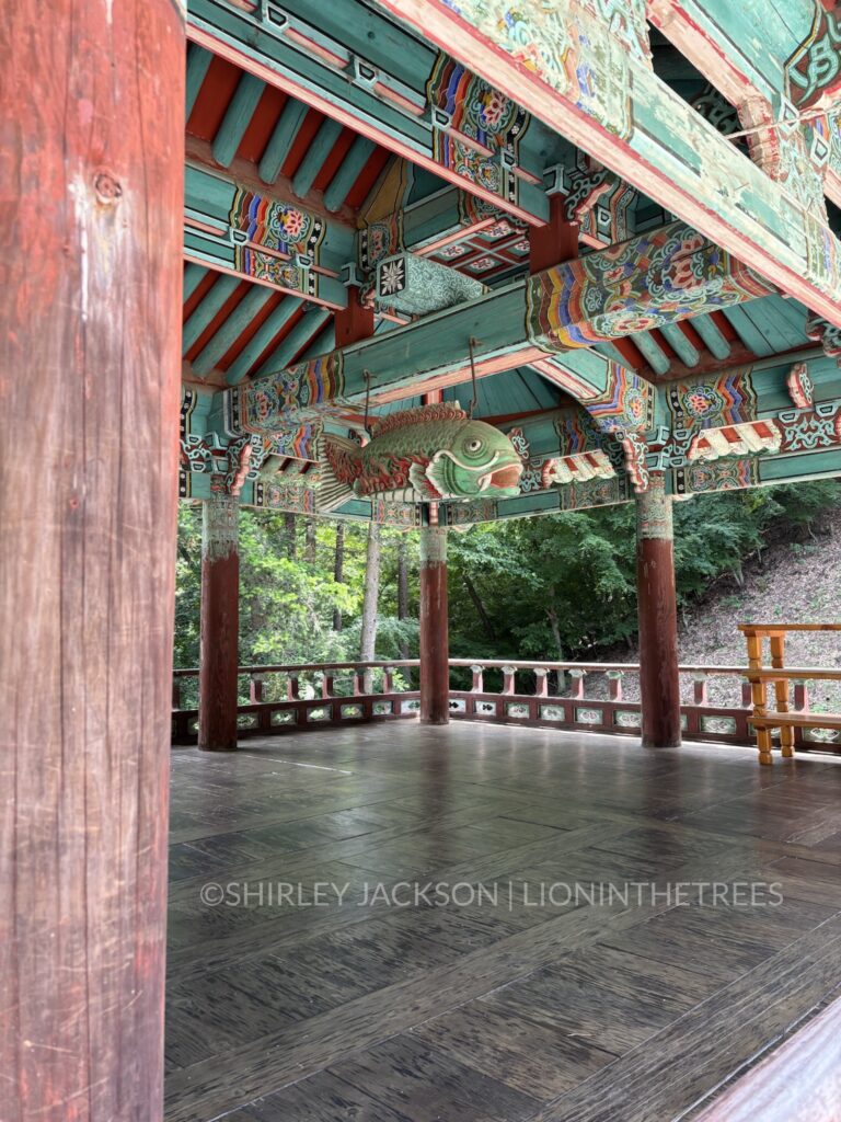 Photo of the interior of a temple building with a giant wooden decorated fish suspended from the ceiling