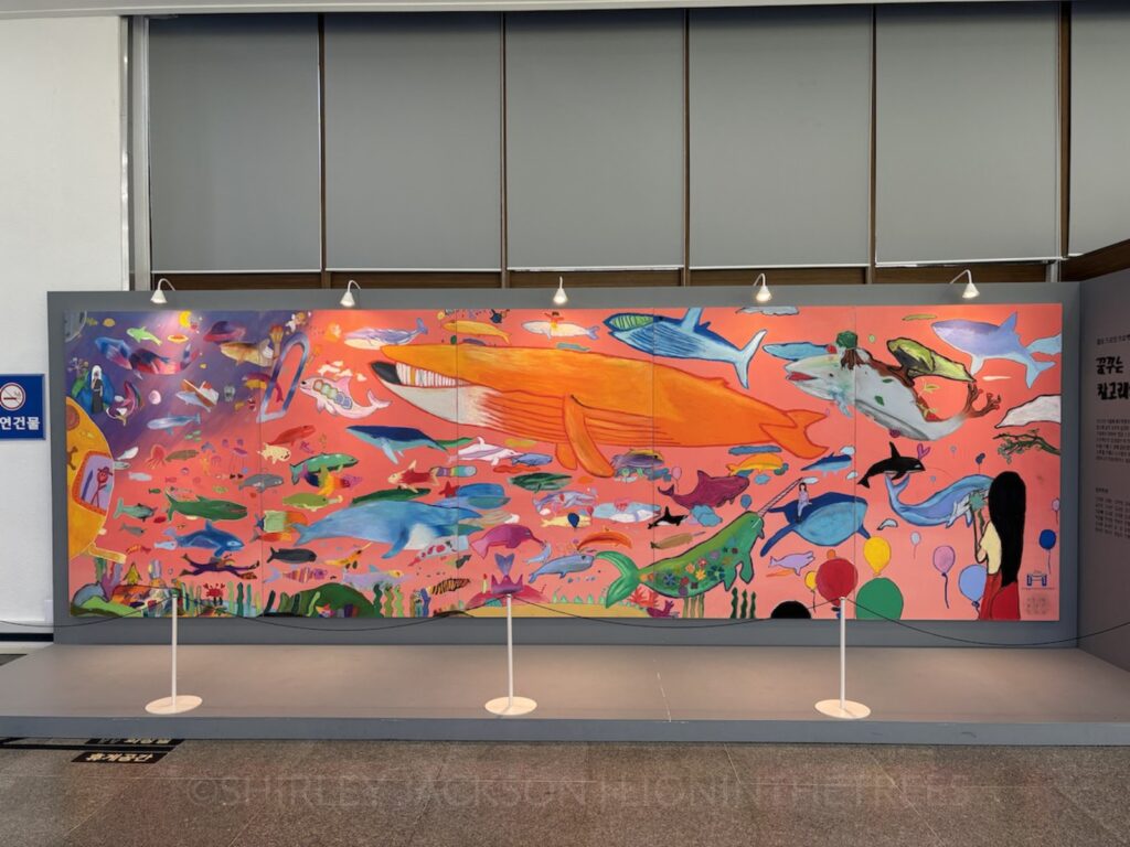 Photo of a beautiful mural that features a variety of whales swimming against a pink, orange background.