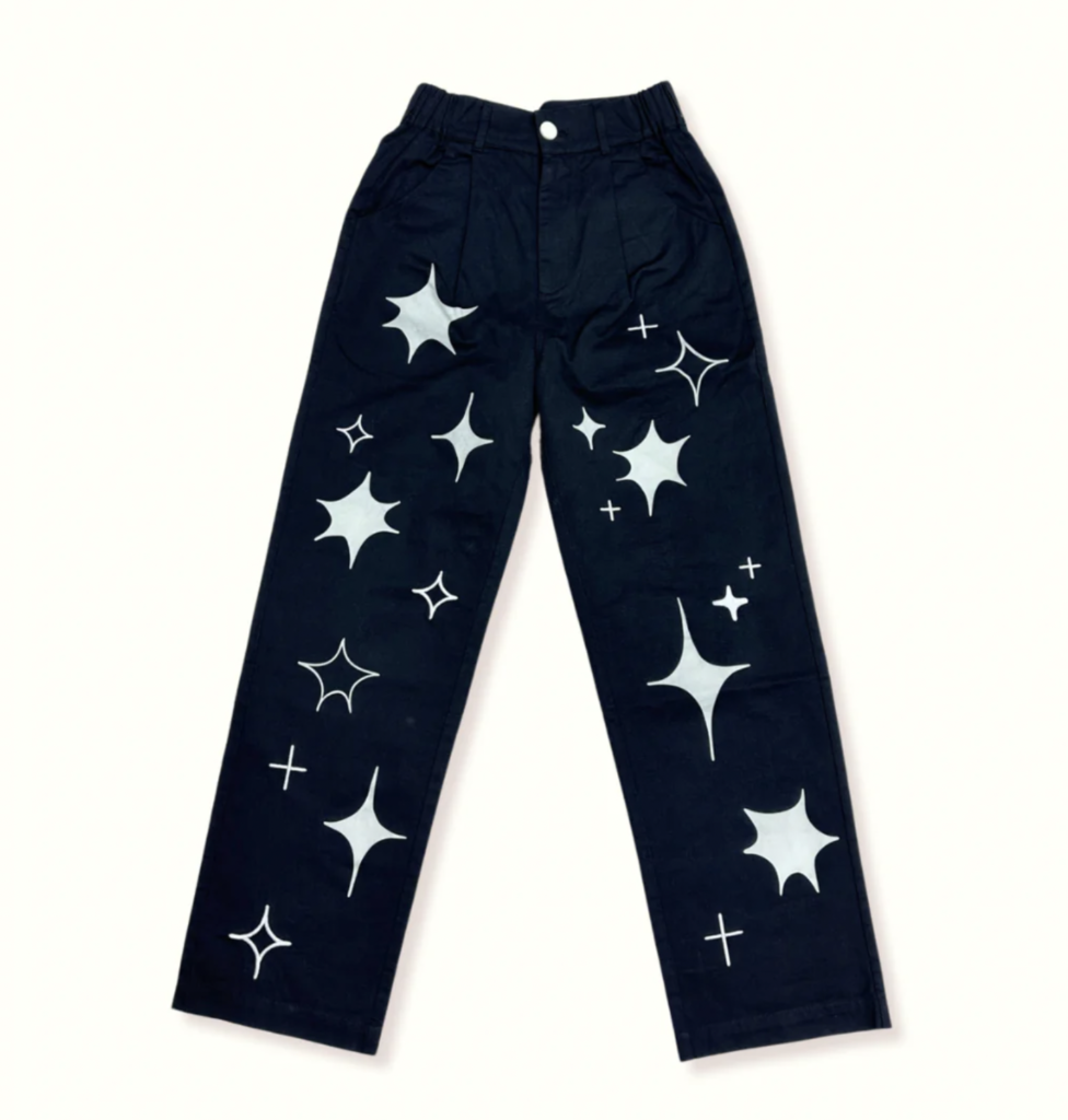 A pair of black pants that feature a white screen-printed sparkle star design on the front of the pant legs. Made by Kojo Jojo Studio.