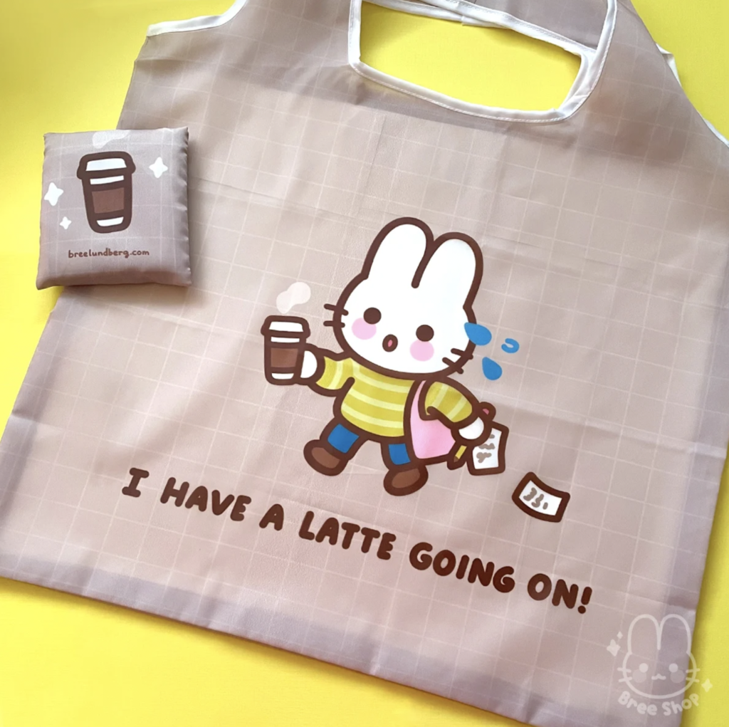 A mocha colour reusable bag featuring a bunny in a hurry with coffee that reads, “I have a latte going on”. Made by Bree Lundberg.