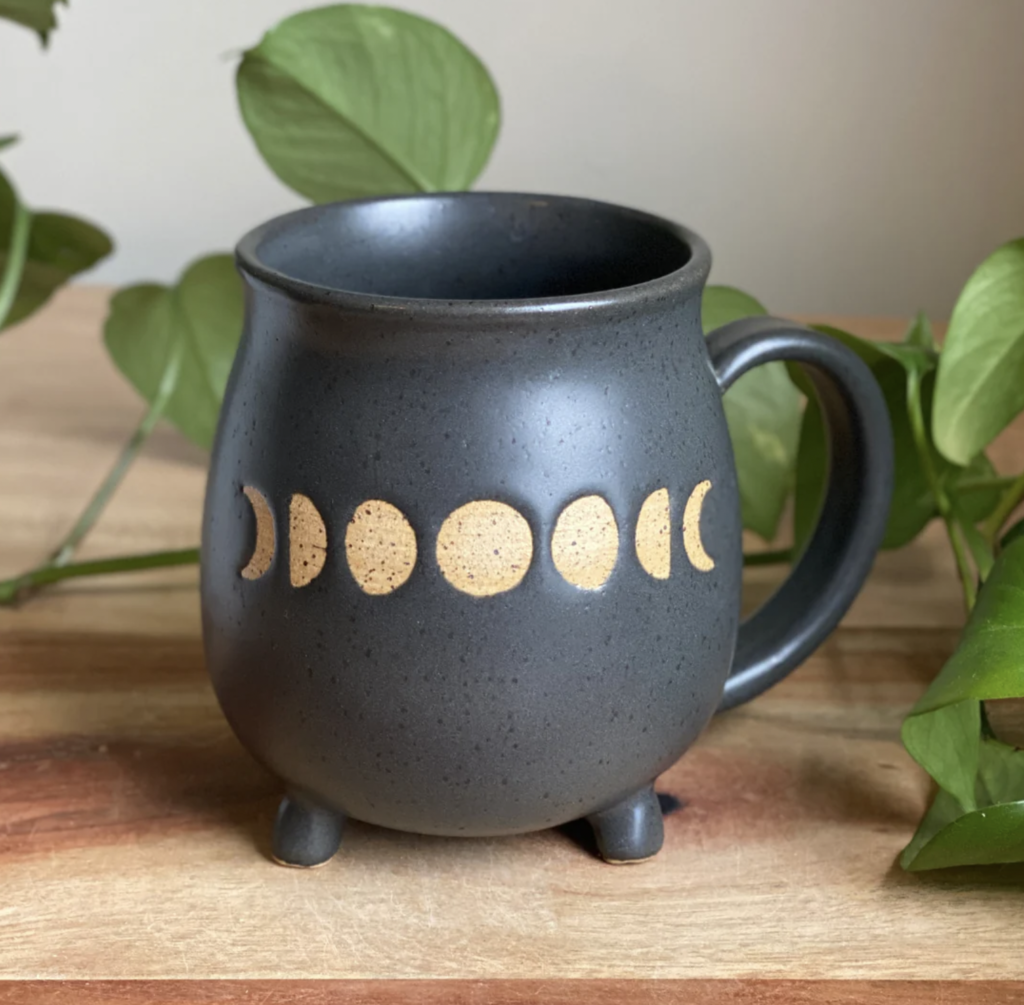 A black cauldron shaped mug that features the cycles of the moon Made by Nissa Arts