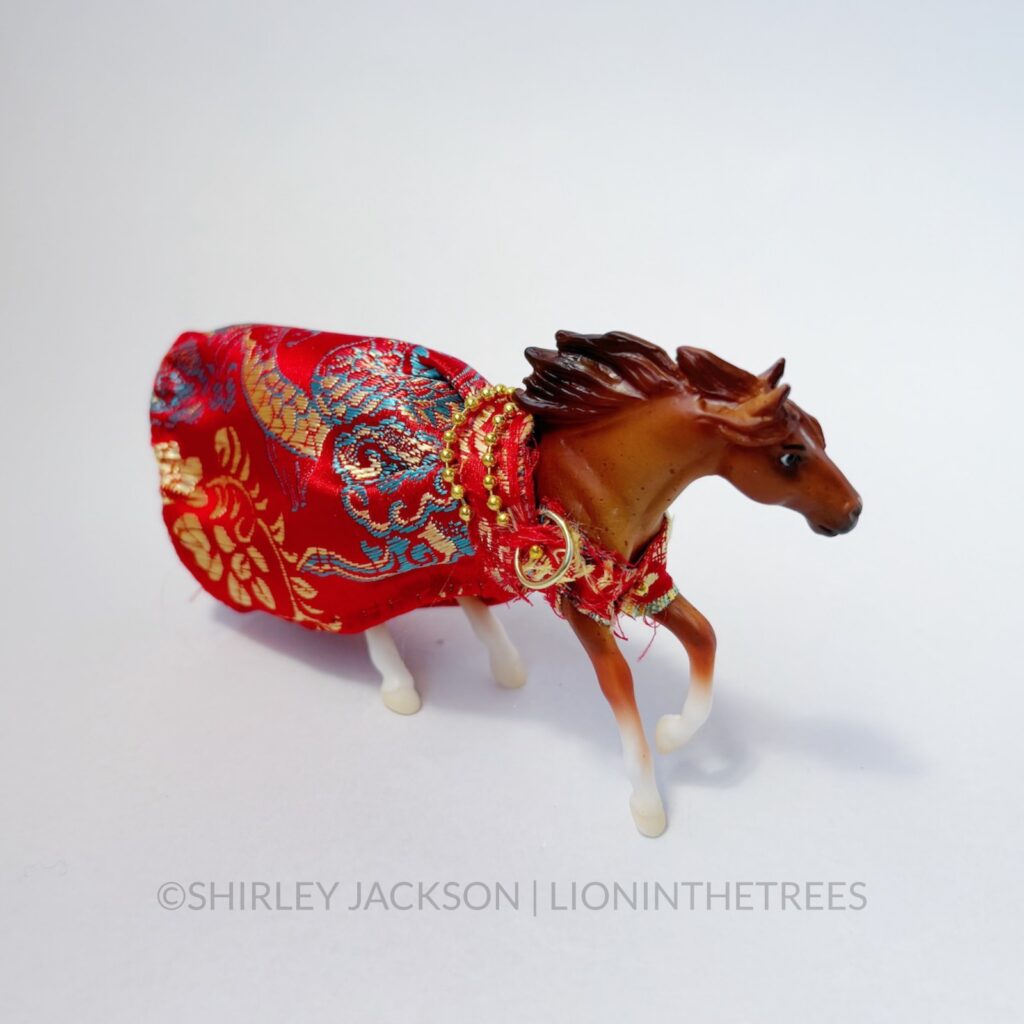 A chestnut horse dressed in a red silk gown with a dragon embroidered pattern.