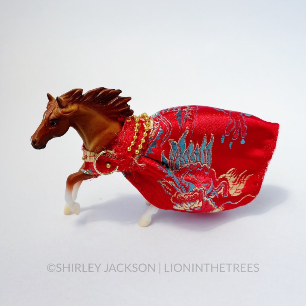 A chestnut horse dressed in a red silk gown with a dragon embroidered pattern.