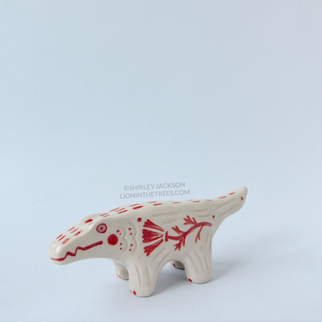 Left side view of the small albino alligator totem. This piece was done with red underglaze details and clear glaze.