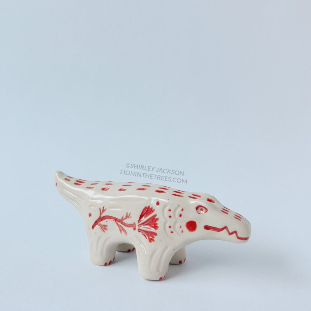 Right side view of the small albino alligator totem. This piece was done with red underglaze details and clear glaze.