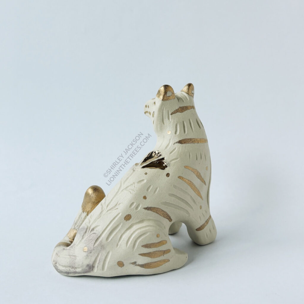 Back 3/4 left side view of the White tiger totem done with no underglaze and gold overglaze in areas detailing the stripes and facial details of the tiger.