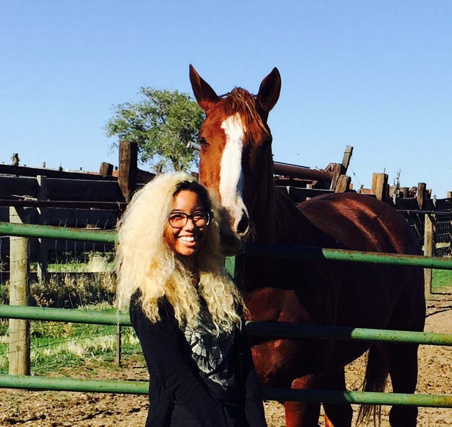 It's a me! I've got platinum blonde hair, a big smile on my face, and a big chestnut horse standing next to me giving me a sniff.