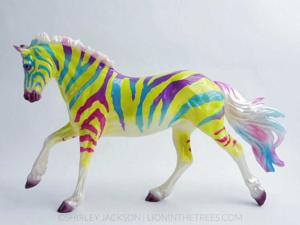 An electric, lime green and purple, turquoise, and magenta red zebra coloured horse done on the Astrid mold.