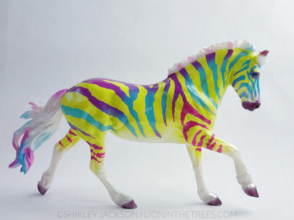 An electric, lime green and purple, turquoise, and magenta red zebra coloured horse done on the Astrid mold.