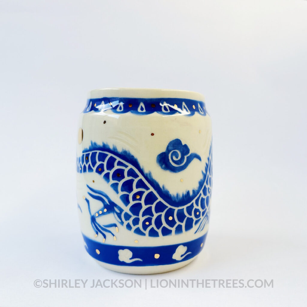 Large sgraffito vessel done with blue underglaze featuring a dragon motif that curls around the entire vessel. There are also gold overglaze details throughout the piece.