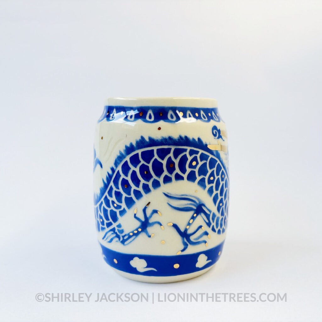 Large sgraffito vessel done with blue underglaze featuring a dragon motif that curls around the entire vessel. There are also gold overglaze details throughout the piece.