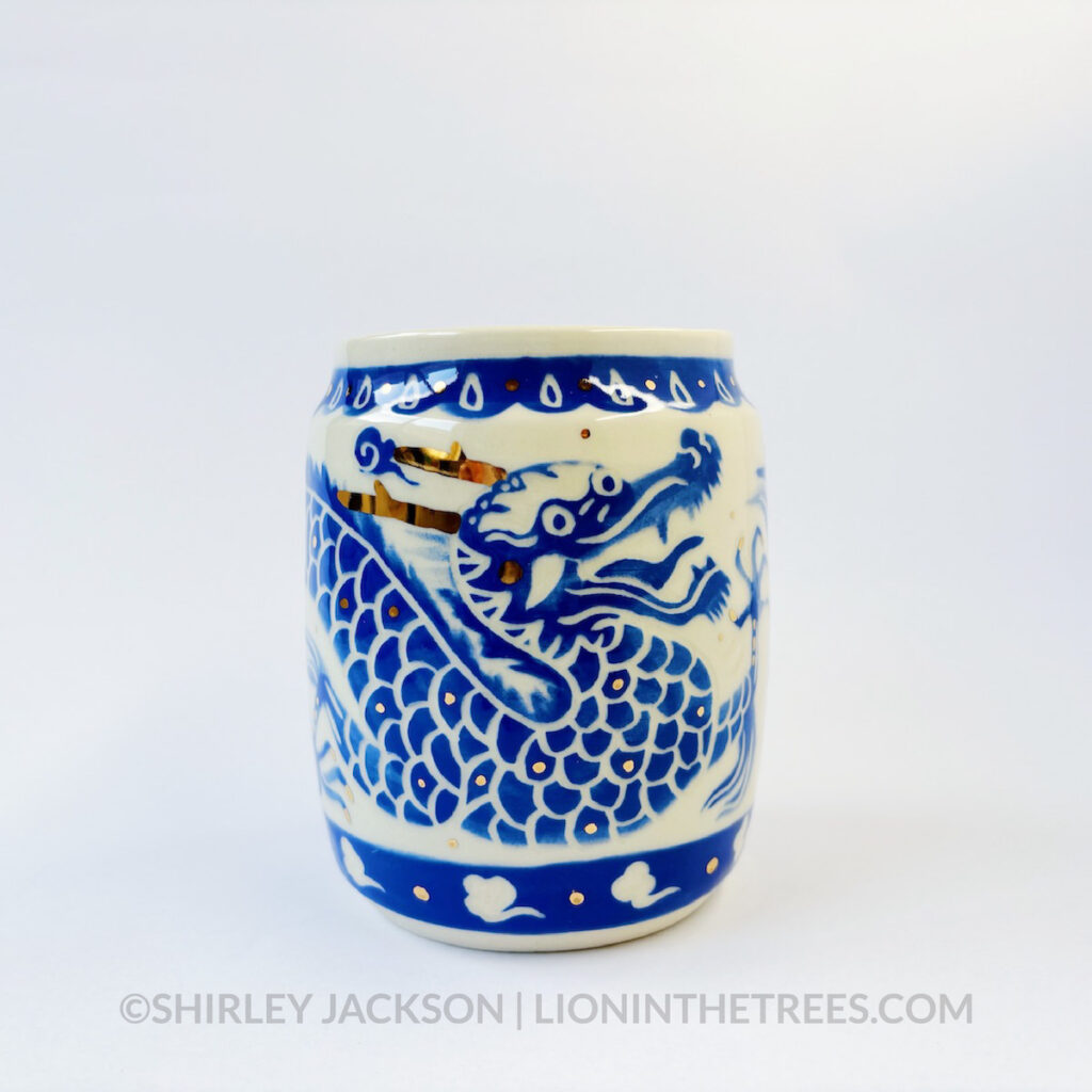 Large sgraffito vessel done with blue underglaze featuring a dragon motif that curls around the entire vessel. There are also gold overglaze details throughout the piece.