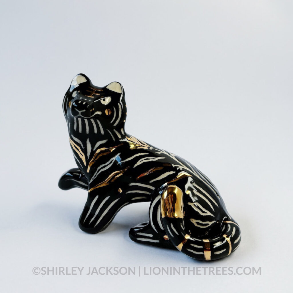 Left side view. Sgraffito Black Tiger totem done with black underglaze and gold overglaze for some of the stripe details. It has one paw up in mid-air.