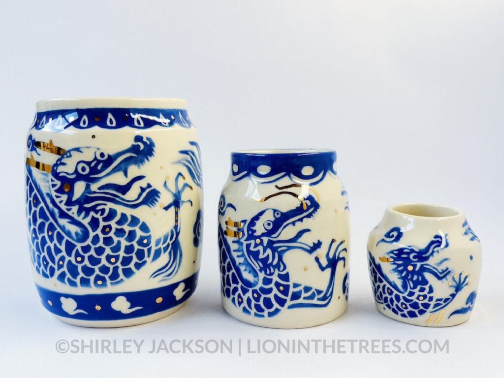 Photo of three ceramic vessels lined up going from large, to medium, to small size. These vessels featured a sgraffito blue underglaze dragon design with gold overglaze details for their whiskers, antlers, and clays.