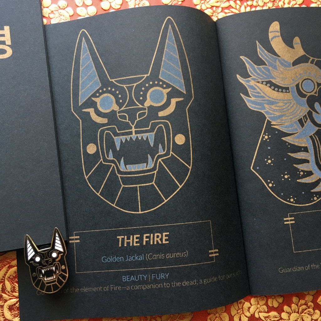 Close-up of my Oracles of the Wild risograph zine. This zine was printed with metallic gold ink and white ink on black paper. This photo portrays the Oracle The Fire, a mask based off of the Golden Jackal.