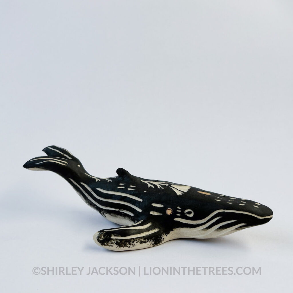 Right 3/4 view. Sgraffito Humpback whale animal sculpture done with black underglaze and gold overglaze for extra details.