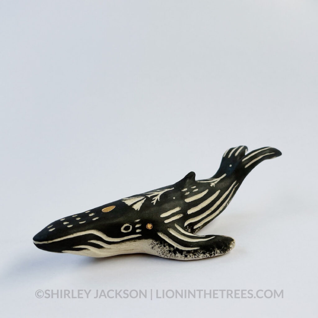 Left 3/4 view. Sgraffito Humpback whale animal sculpture done with black underglaze and gold overglaze for extra details.