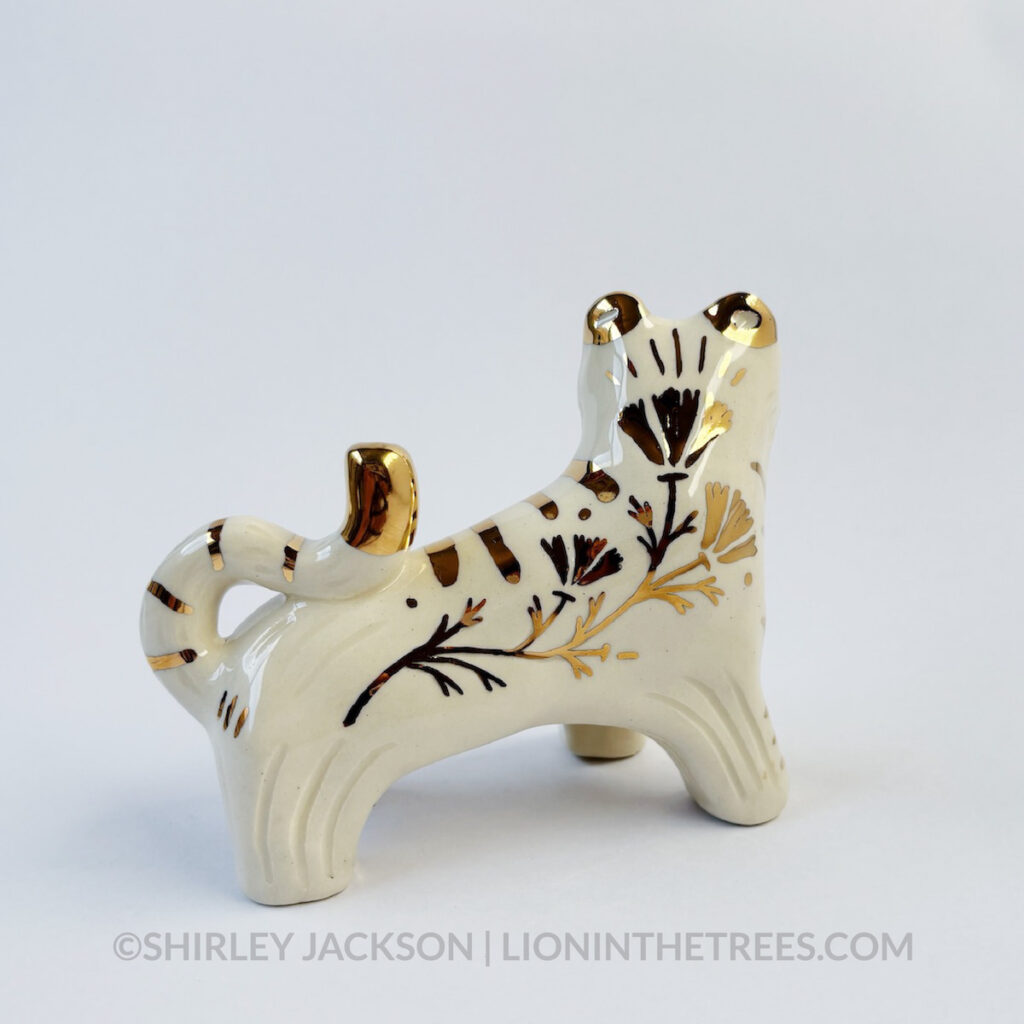 Back view of a sgraffito white tiger ceramic sculpture with gold overglaze details that make up the stripes, other markings, and my signature California Poppy motif on the side of it's body.