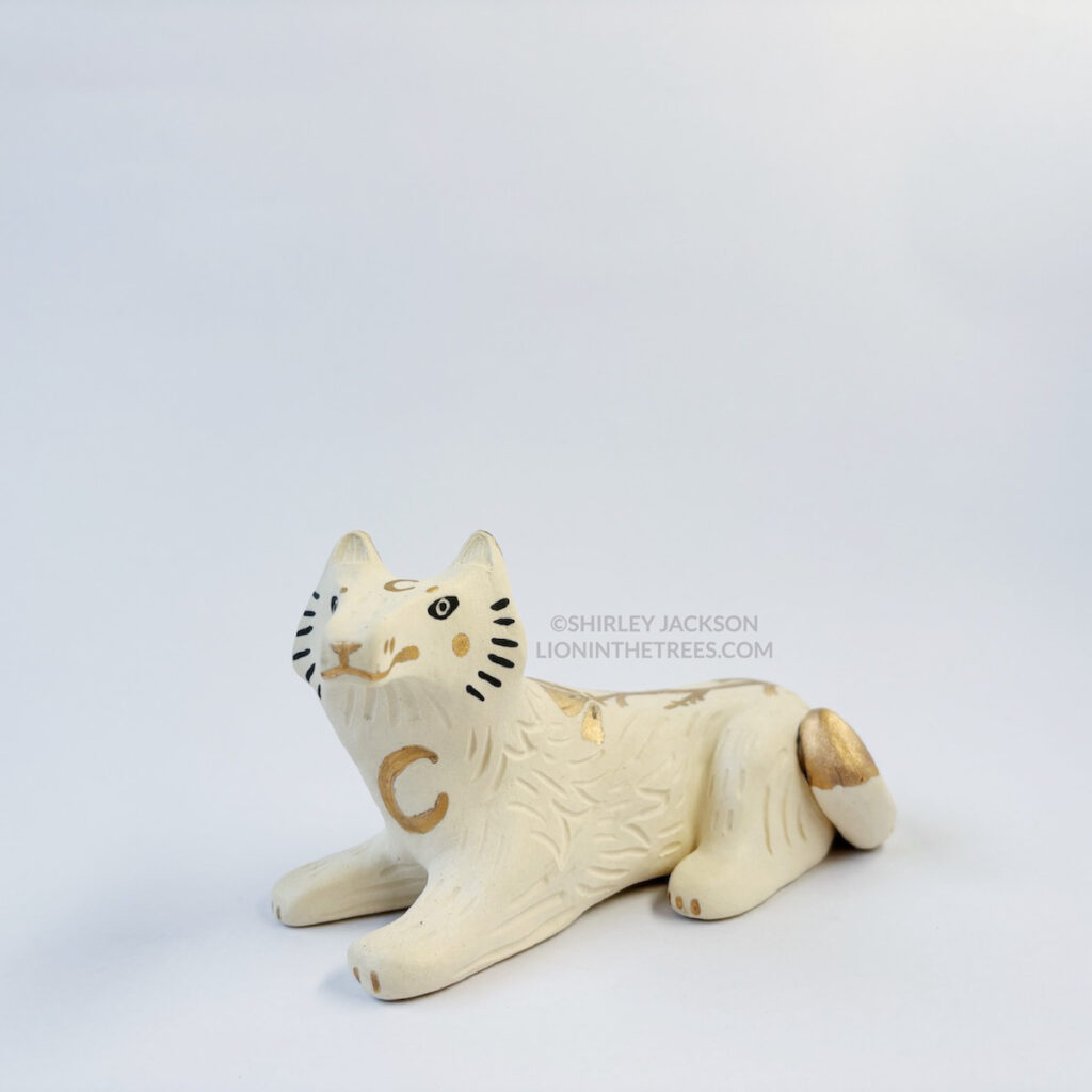 Front view of a sgraffito white wolf ceramic sculpture with gold overglaze details such as crescent moons, and my signature California Poppy motif on the top of it's body.