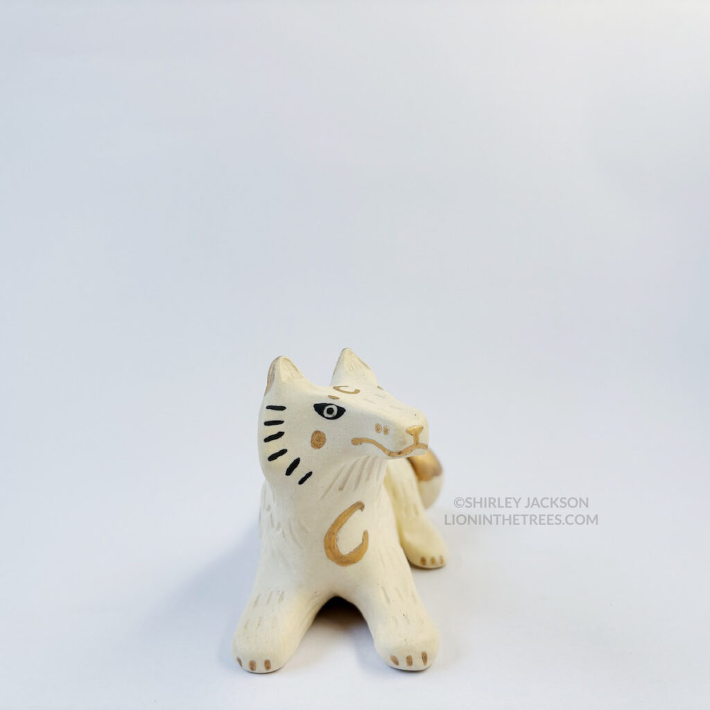 Front view of a sgraffito white wolf ceramic sculpture with gold overglaze details such as crescent moons, and my signature California Poppy motif on the top of it's body.