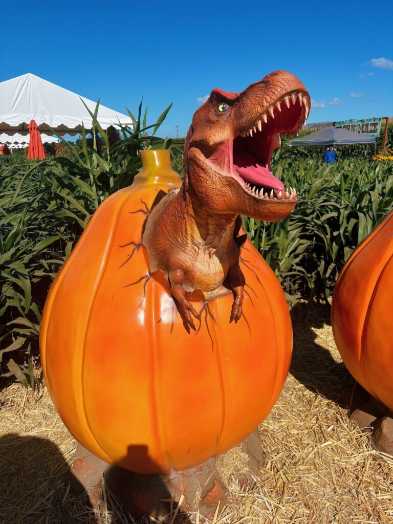 A baby t-red popping out of a pumpkin