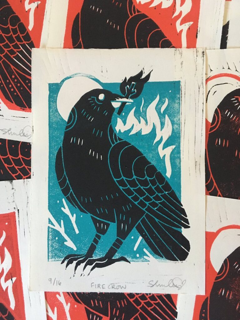 Linoblock relief print featuring a crow with a stick on fire in it's mouth. This print was done with a red background colour.