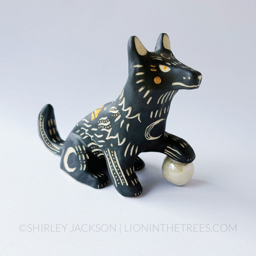 Black and orange underglazed sgraffito wolf totem. She has a paw protecting a shiny orb.