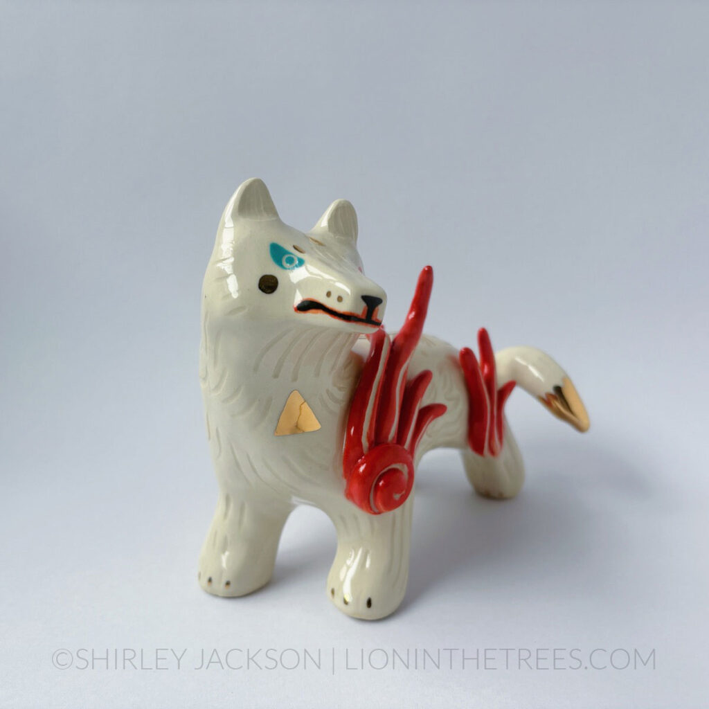 White sgraffito wolf with gold overglaze details. They have heterochromia eyes - one red and one turquoise - along with red flames coming off their shoulders and thighs.