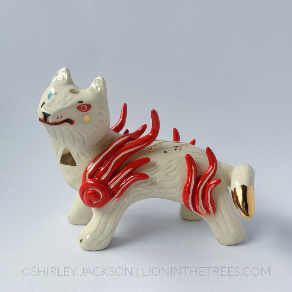 White sgraffito wolf with gold overglaze details. They have heterochromia eyes - one red and one turquoise - along with red flames coming off their shoulders and thighs.