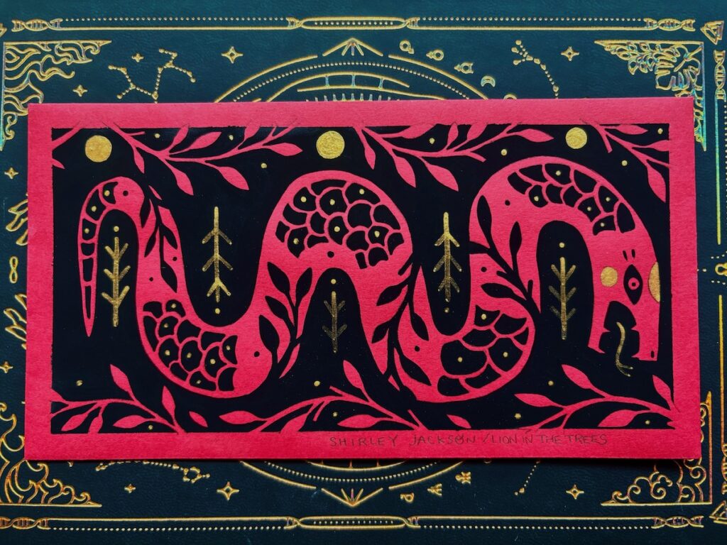 A horizontal painting done with black and gold paint on a red envelope used during Lunar New Year celebrations. The painting features a snake with floral details surrounding it and blending into it’s body.