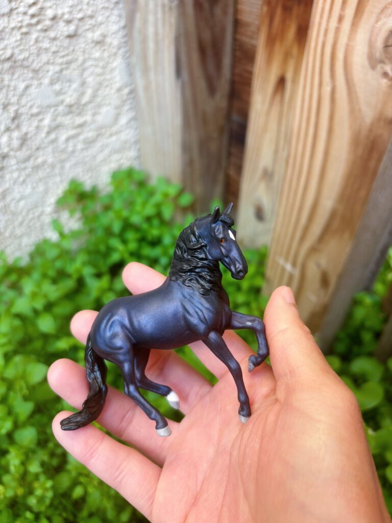 Photo of the horse in my hand to show it's scale. It's very small and can fit in my palm. You can also see more of the purple/blue effect in it's coat.