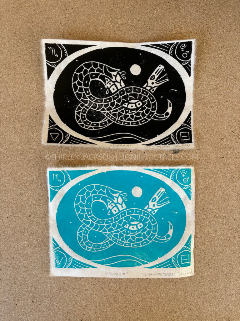 Photo showing two block prints of my snake Scorpio design. The top print was done with black ink and the print on the bottom was done with a turquoise ink.