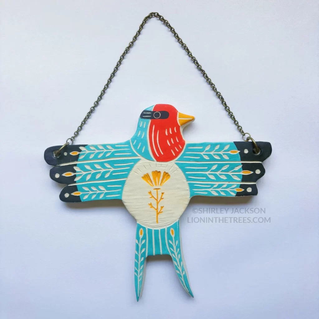 A ceramic wall slab in the shape of a t-posed Barn Swallow featuring sgraffito floral design elements.