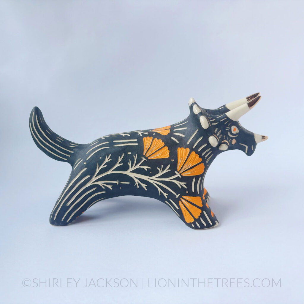 Black sgraffito Triceratops totem done with various underglaze, clear glaze, and gold luster.