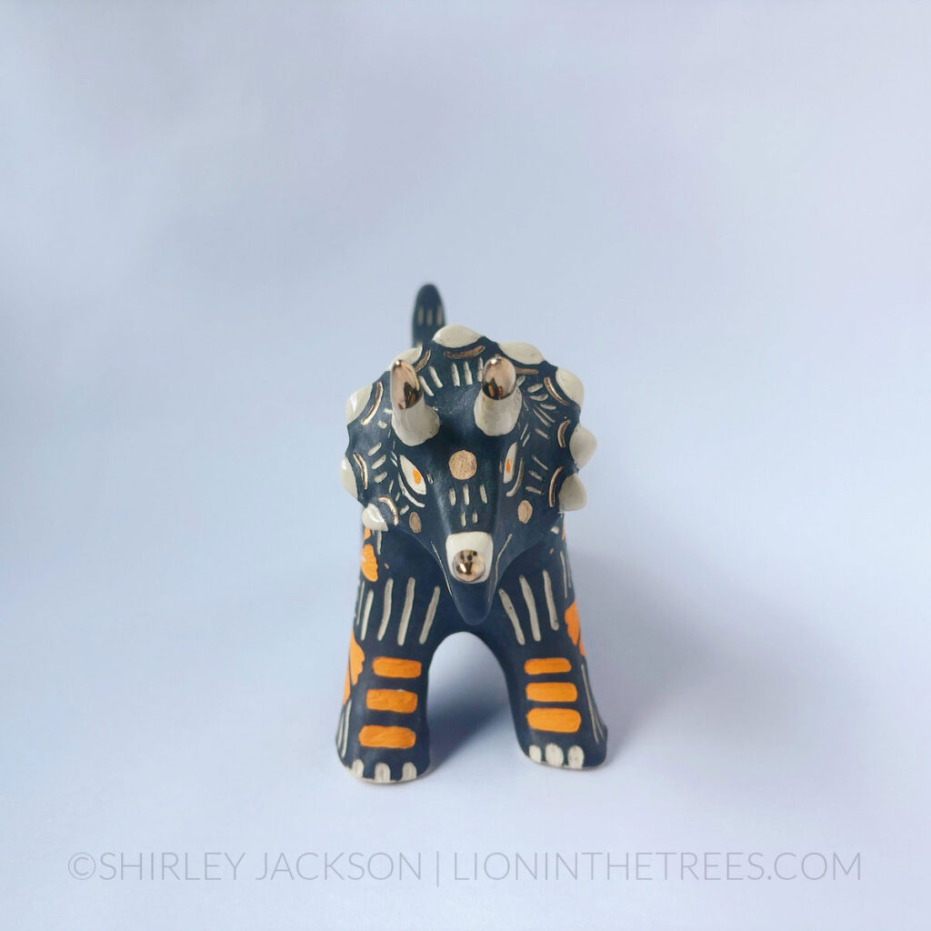 Black sgraffito Triceratops totem done with various underglaze, clear glaze, and gold luster.